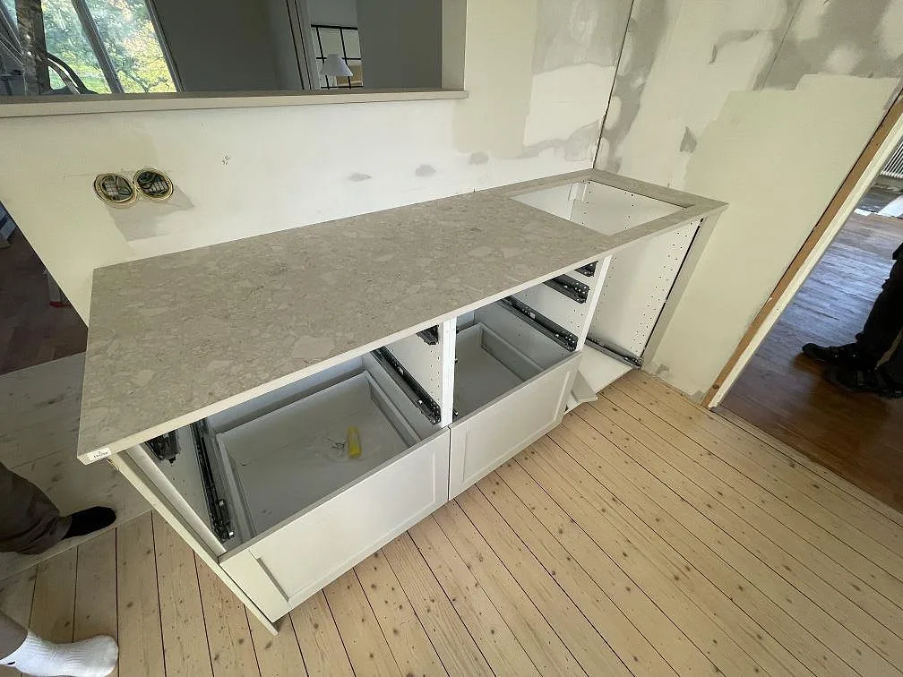 Lång köksbänkskiva i matt Dekton Ava på vita stommar, med ljus keramikyta och väggnära montering i Karlskoga.
