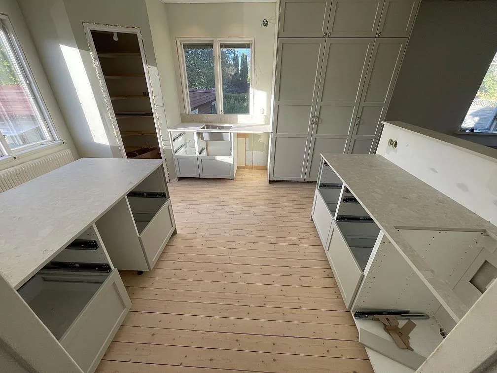 Flera köksbänkskivor i matt Dekton Ava med ljus ådring monterade längs väggarna i ett kök i Karlskoga.
