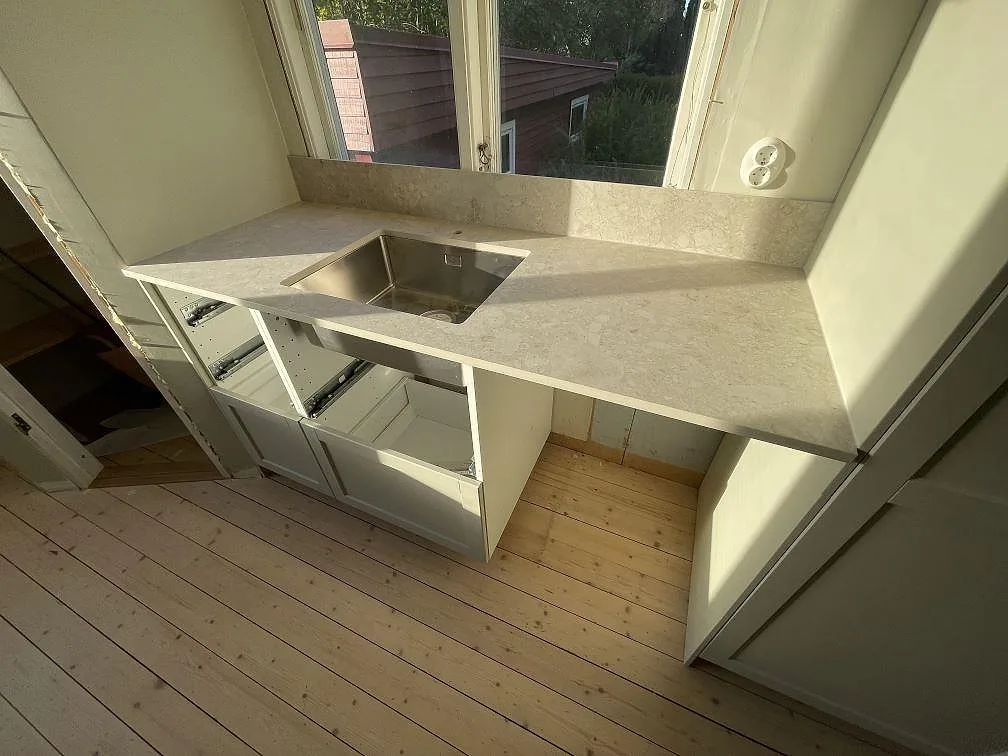 Köksbänkskiva i matt Dekton Ava med synlig diskho och uppvikt stänkkant vid fönster i Karlskoga.