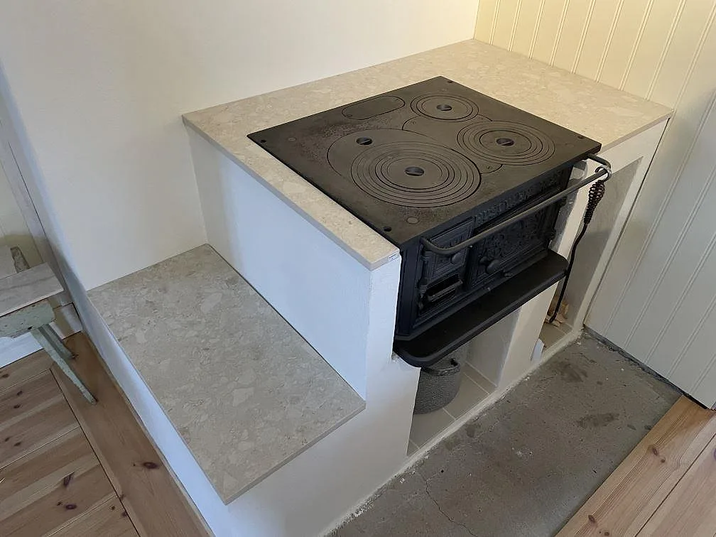 Detalj av matt Dekton Ava i ljus keramik monterad runt vedspis och sidobänk i köket i Kristinehamn.