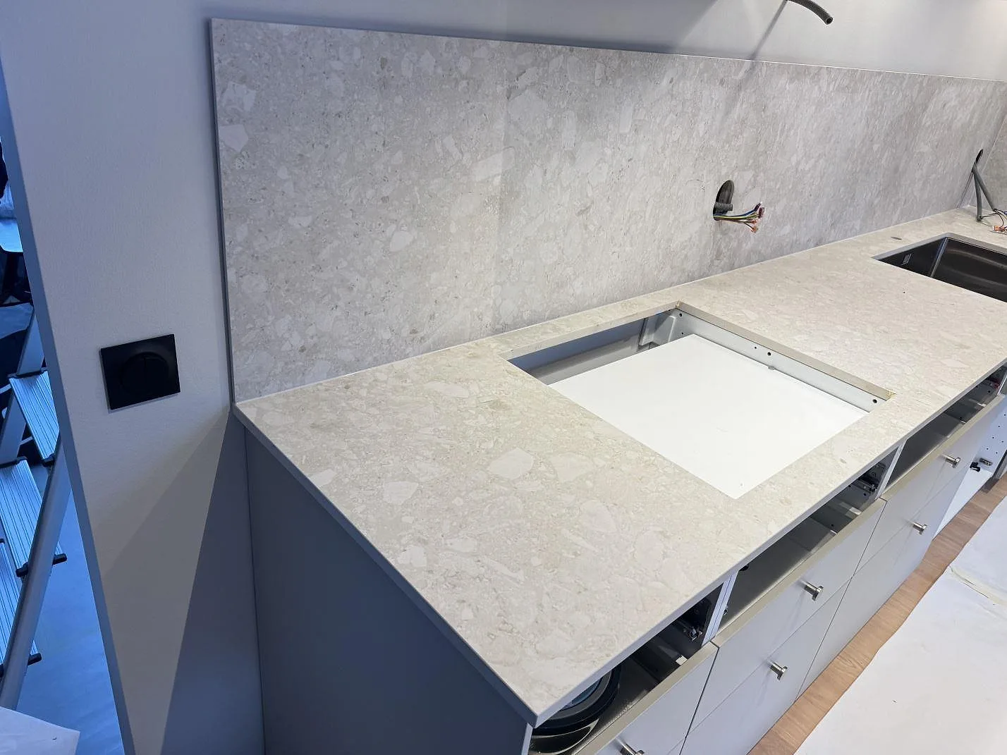 Köksbänkskiva i matt Dekton Ava, varm gräddvit keramik med ceppomönster, lång bänkrad med urtag för häll och rostfri diskho samt stänkskydd i samma sten i ett kök i Landskrona.