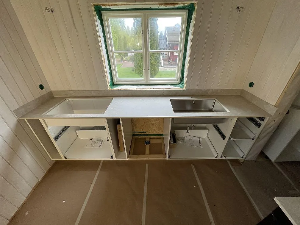 Köksbänkskiva i matt Dekton Ava, ljus grågrön keramik, med underlimmad rostfri diskho under fönstret i ett kök i Mora.