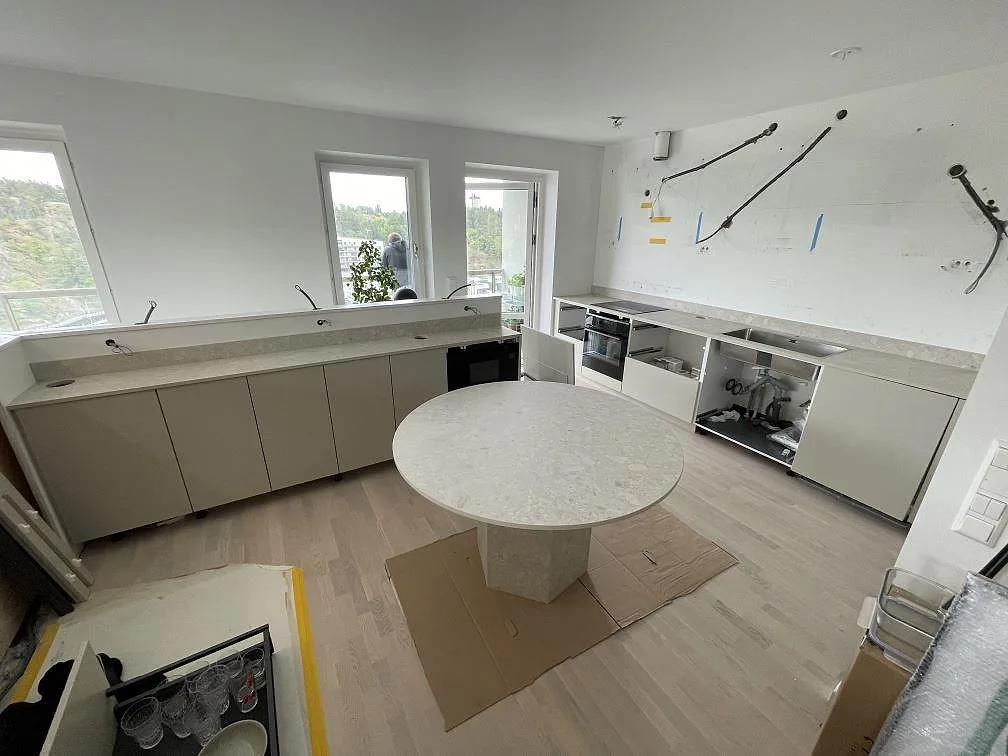 Köksbänkskiva i matt Dekton Ava med rak väggbänk, rund central arbetsyta och stänkskydd i ett kök i Nacka.