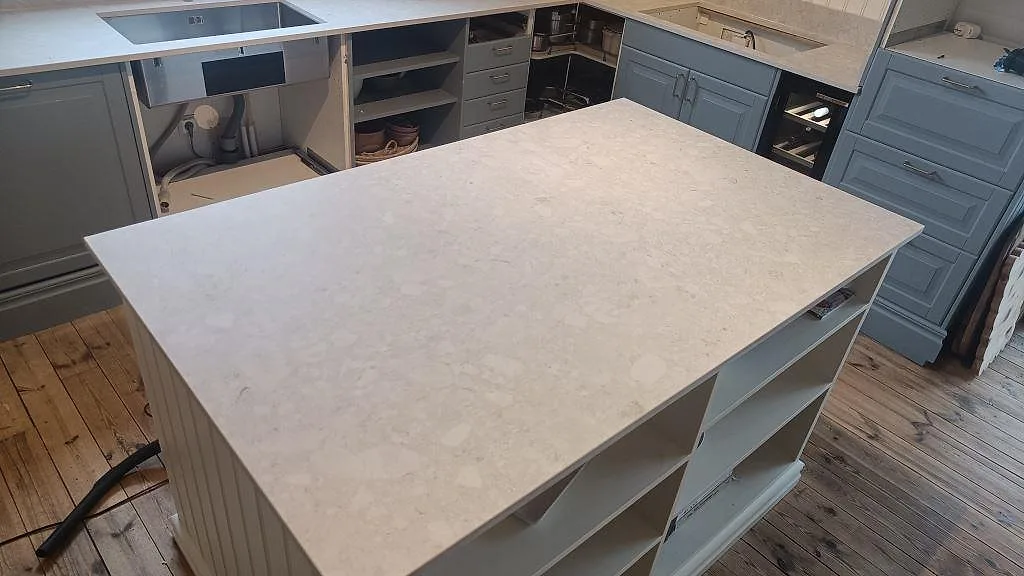 Närbild på köksö i matt Dekton Ava, keramik, med bänkskivor och blå köksstommar i Nässjö.