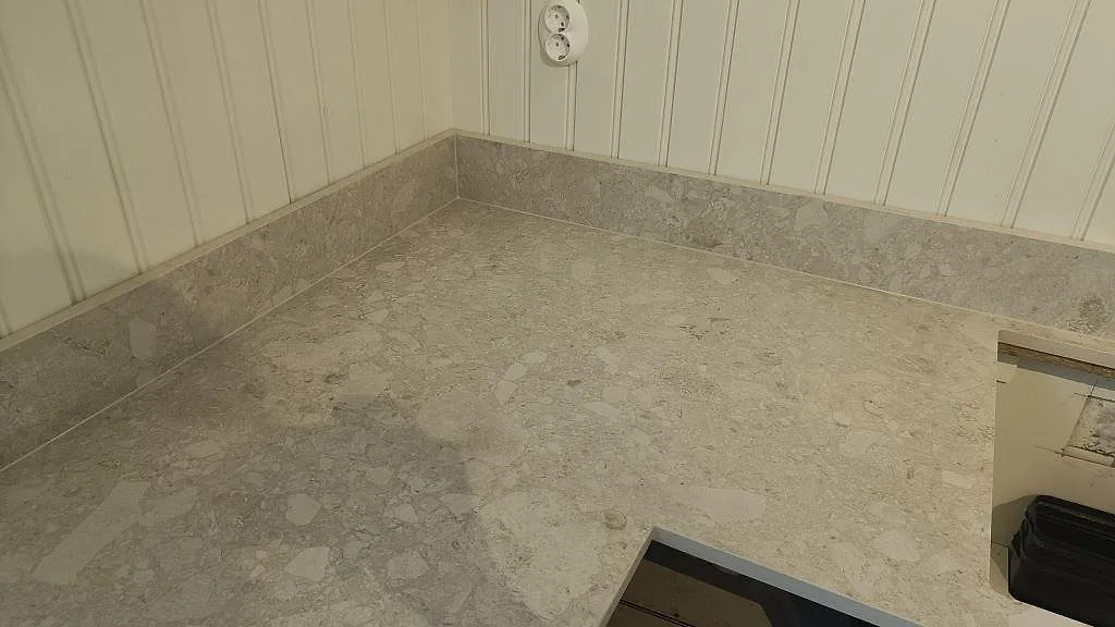 Närbild på hörn och arbetsyta i matt Dekton Ava, keramik, med stänkkant mot panelvägg i Nässjö.