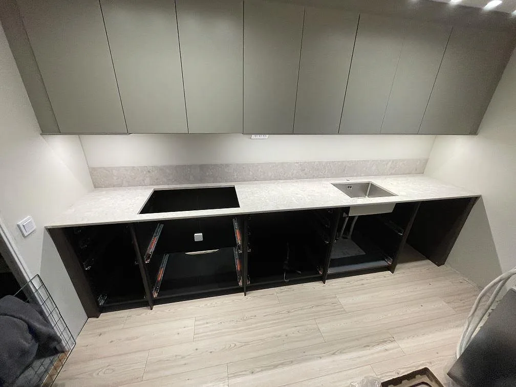 Köksbänkskiva i matt Dekton Ava, ljus keramik, med urtag för häll, underlimmad rostfri diskho och stänkskydd i ett kök i Strövelstorp.