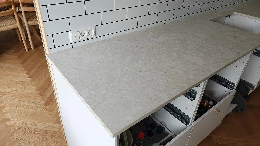 Köksbänkskiva i matt Dekton Ava keramik med ljus stenbild, kaklad vägg och öppen skåpstomme i ett kök i Tåstrup.