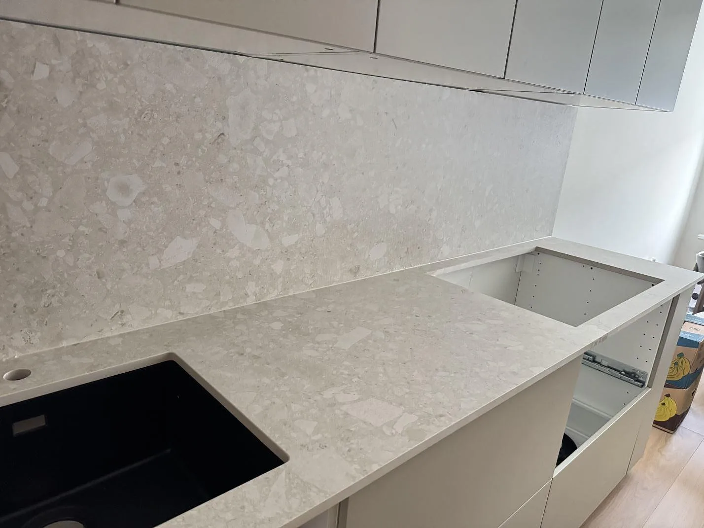 Köksbänkskiva i matt Dekton Ava keramik med stänkskydd i samma sten, synlig diskho och förberett hällurtag i ett kök i Växjö.