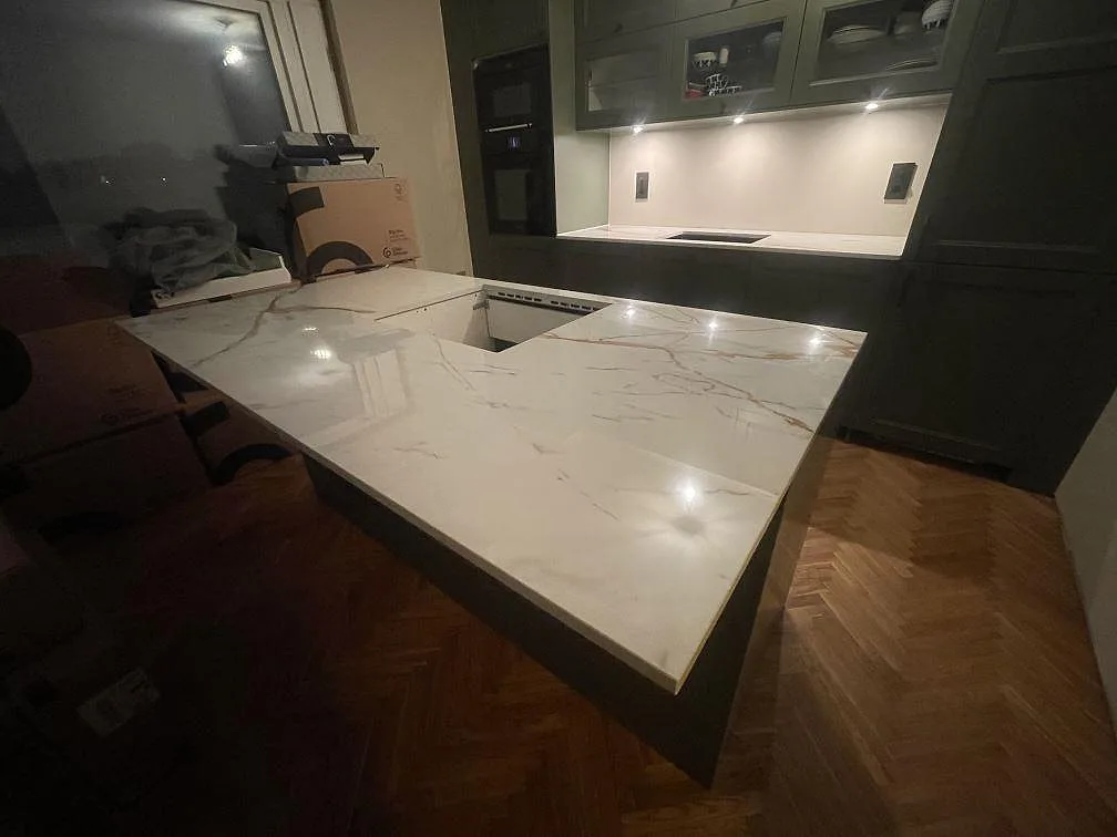 Polerad köksö i vit Dekton Awake med gyllene ådring och urtag för häll i ett salviagrönt kök i Enskede.