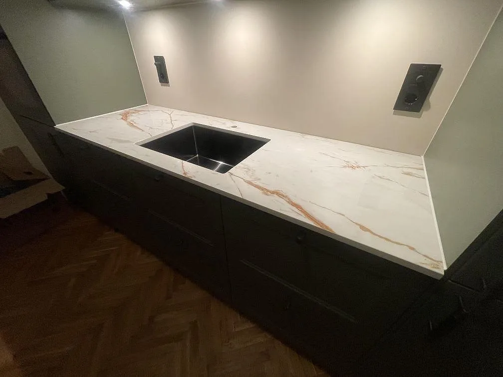 Köksbänk i vit Dekton Awake med underlimmad rostfri diskho och uppvikt stänkskydd i samma sten i ett kök i Enskede.