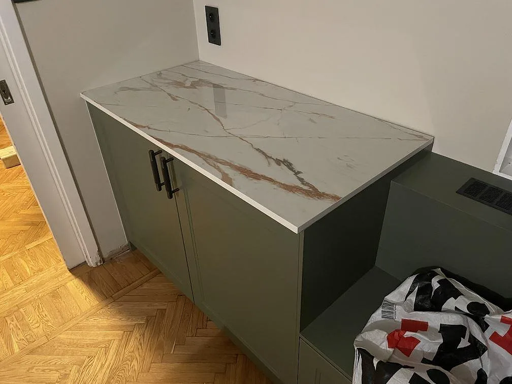 Polerad bänkskiva i Dekton Awake med rostfärgad ådring ovanpå ett grönt köksskåp med svart bygelhandtag i ett kök i Enskede.