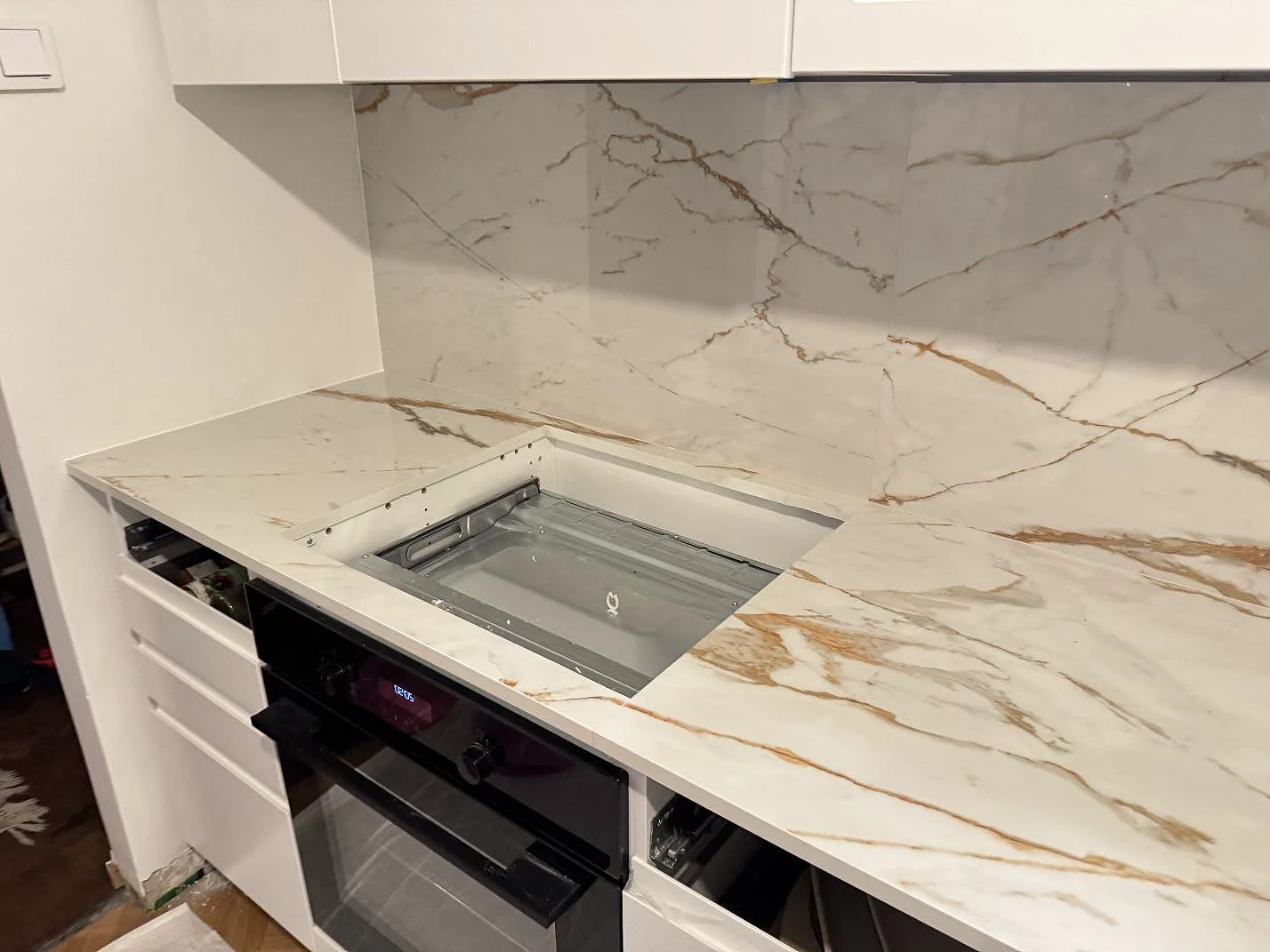 Hällurtag i en köksbänkskiva av polerad Dekton Awake med inbyggd ugn under, vit keramik med guldådring i ett kök i Göteborg.