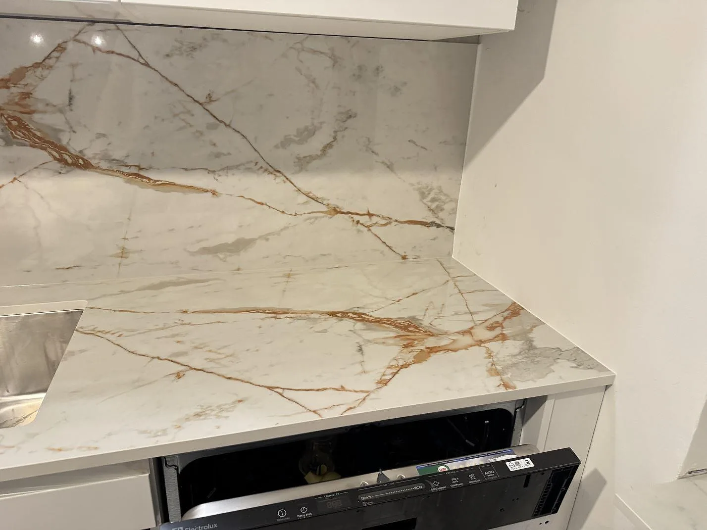 Köksbänkskiva i vit Dekton Awake med varm guldådring, polerad, i ett hörnkök i Göteborg med uppvikt heltäckande stänkvägg i samma sten och underlimmad rostfri diskho.