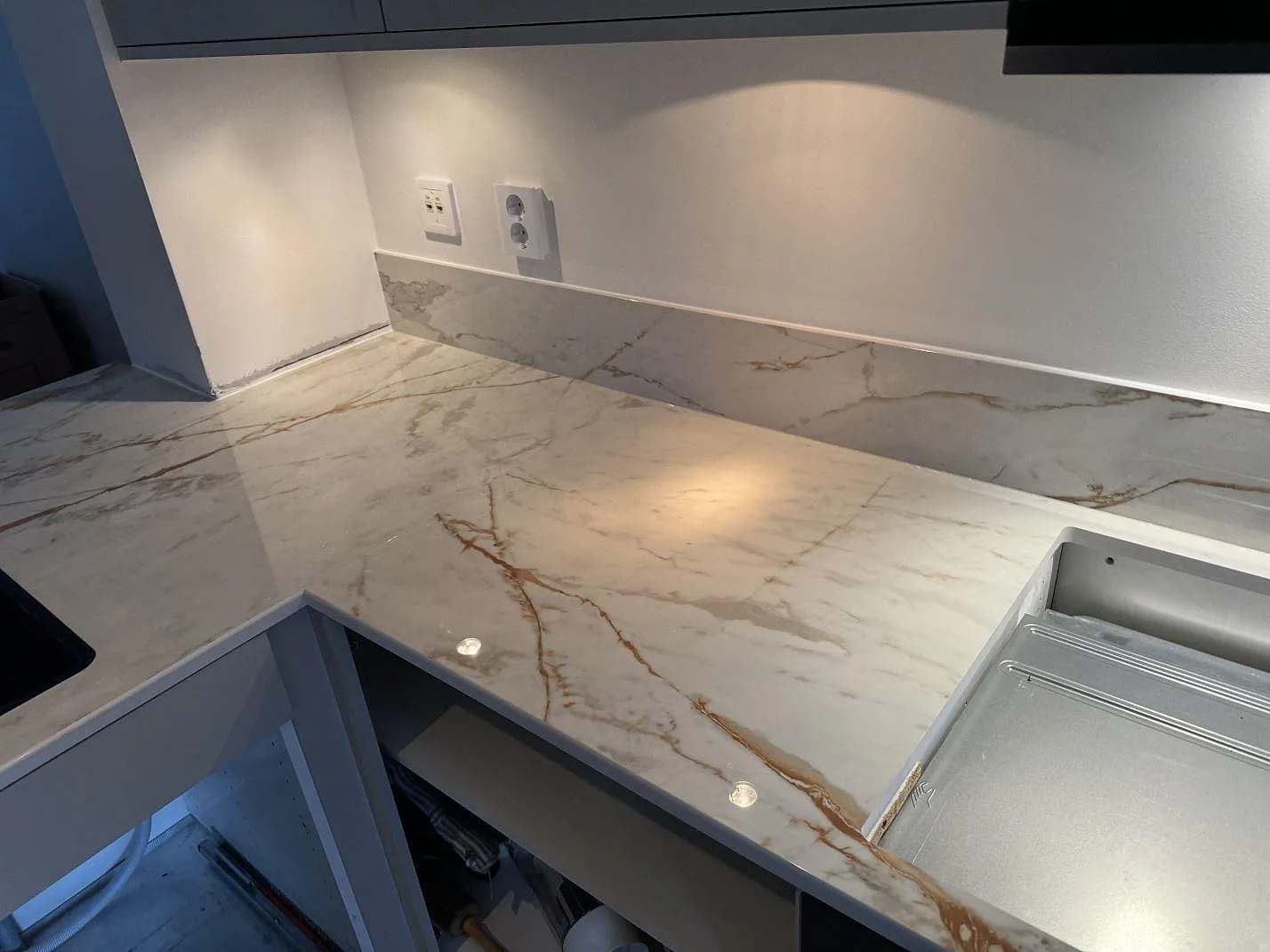 L-formad köksbänkskiva i polerad Dekton Awake med stänkskydd och tydlig ådring runt diskzonen i Limhamn.