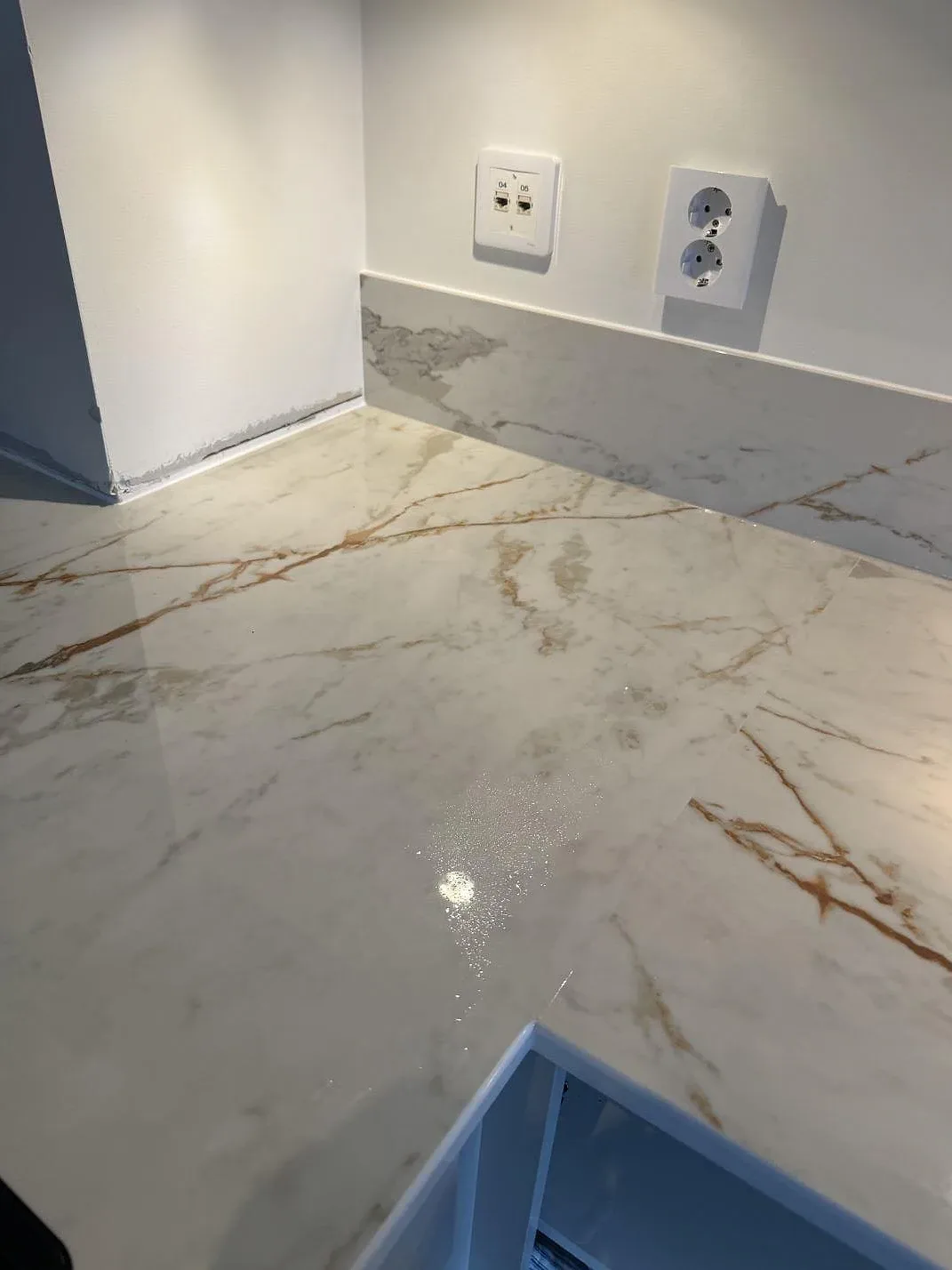 Detaljbild av polerad Dekton Awake med stänkskydd, vägguttag och blanka reflexer i ett kök i Limhamn.