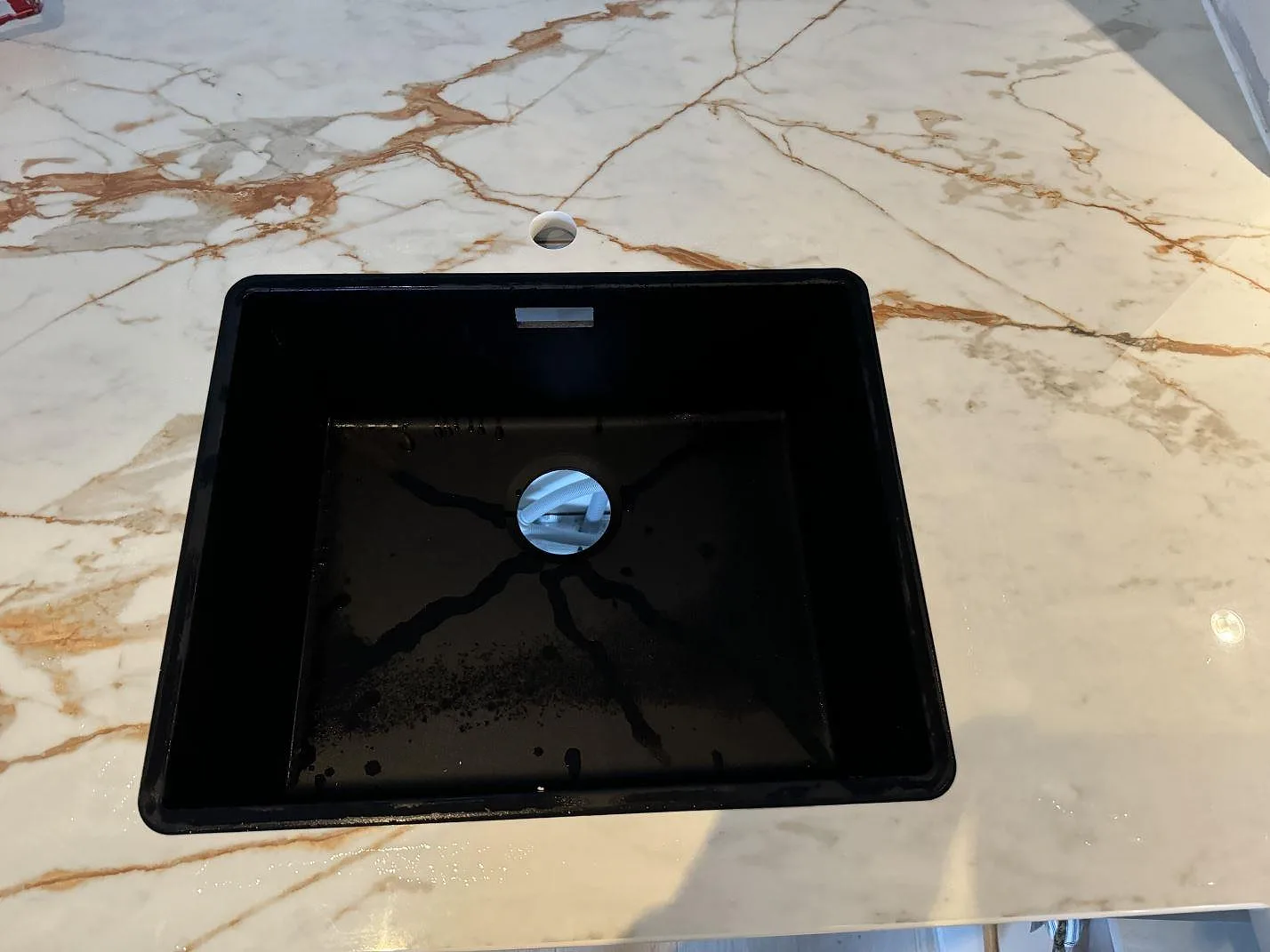 Närbild av svart diskho i polerad Dekton Awake med tapphål och varm ådring i ett kök i Limhamn.