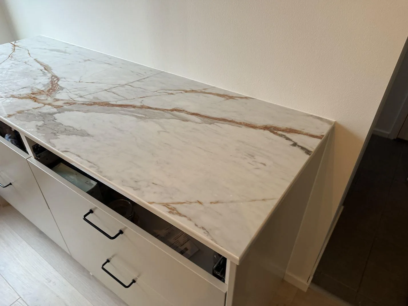 Lång bänkrad i polerad Dekton Awake med 8 mm stänkskydd, vita köksstommar och ljus vägg i Limhamn.