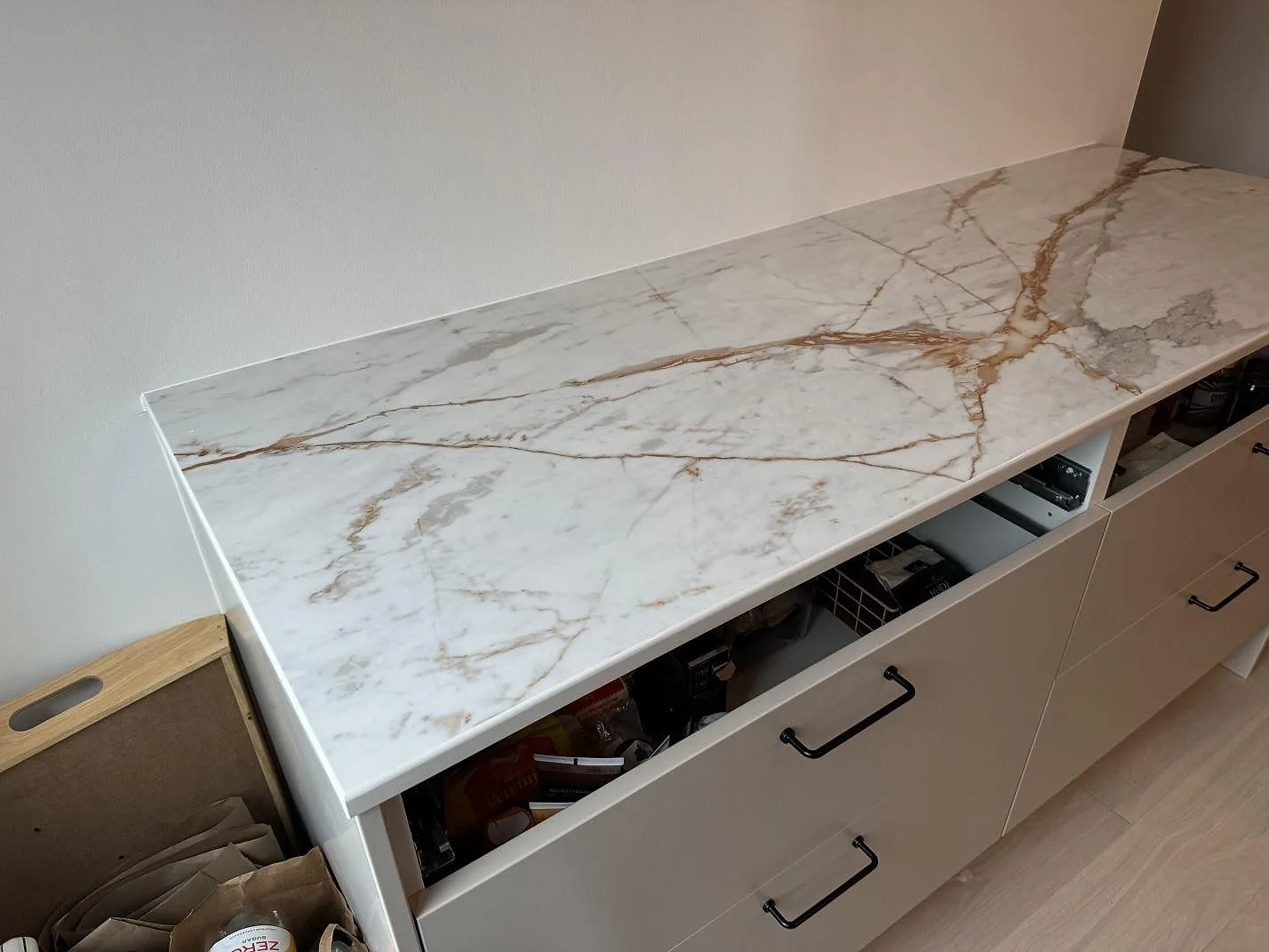 Sidovy av lång köksbänkskiva i polerad Dekton Awake med varm ådring och öppna köksstommar i Limhamn.