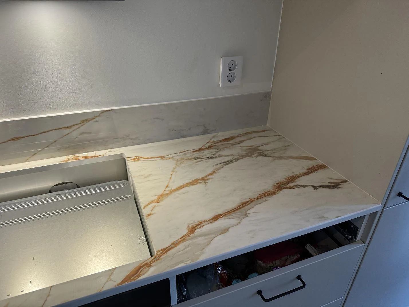 Detalj av polerad Dekton Awake som köksbänkskiva med låg stänkkant, eluttag och ljus ådring i Limhamn.