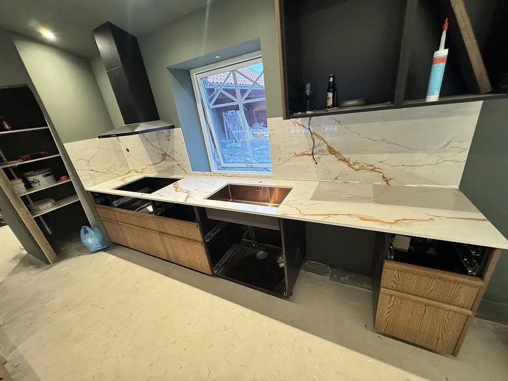 Bred vy över köksbänkskiva i polerad Dekton Awake med stänkskydd, diskho och öppning för häll i ett kök i Osby.