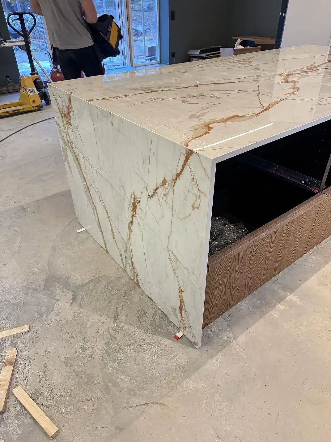 Sidovy av köksö i polerad Dekton Awake med fallande gavel, vit keramik och rostfärgad ådring, under montering i Osby.