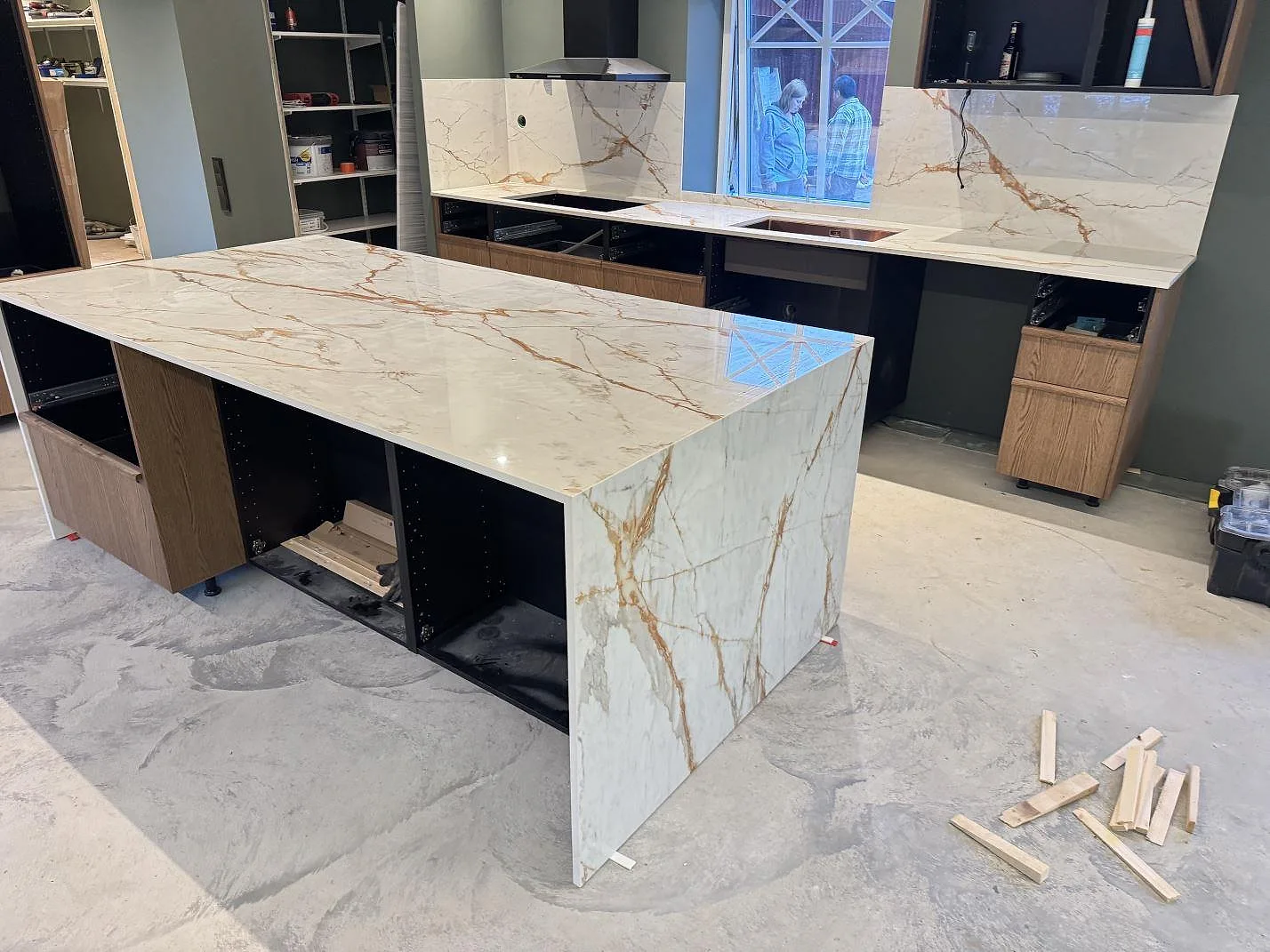 Köksö och väggbänk i polerad Dekton Awake, vit keramik med rostfärgad ådring och stänkskydd, under montering i ett kök i Osby.