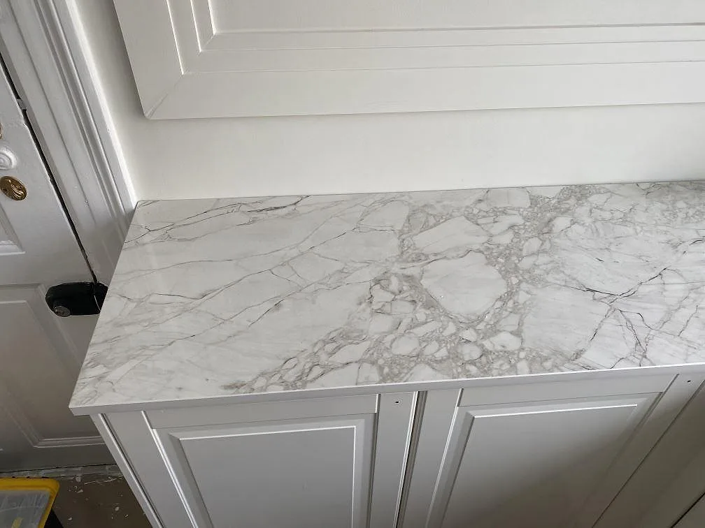 Bänkskiva i vit Dekton Bergen mot vit pärlspontvägg i ett kök i Frederiksberg, polerad yta med naturlig ådring.