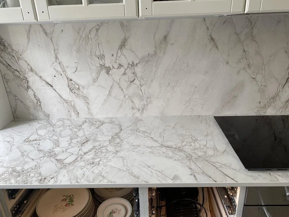 Heltäckande stänkvägg och bänkskiva i polerad Dekton Bergen med infälld häll i ett kök i Frederiksberg.