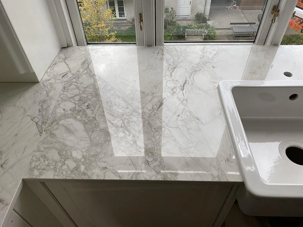 Köksbänkskiva i Dekton Bergen vid fönster i Frederiksberg med vit underlimmad keramikho i den polerade stenen.