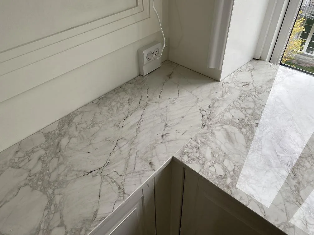 Polerad Dekton Bergen bänkskiva i hörnläge mot fönster i ett kök i Frederiksberg, med tydlig grå ådring i den vita keramiken.