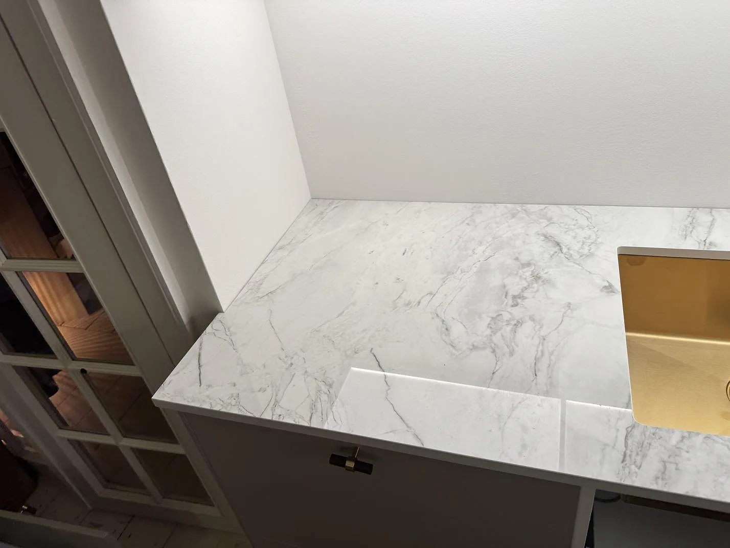 Sidovy av polerad Dekton Bergen köksbänkskiva vid diskho och lucka under montering i Frederiksberg.
