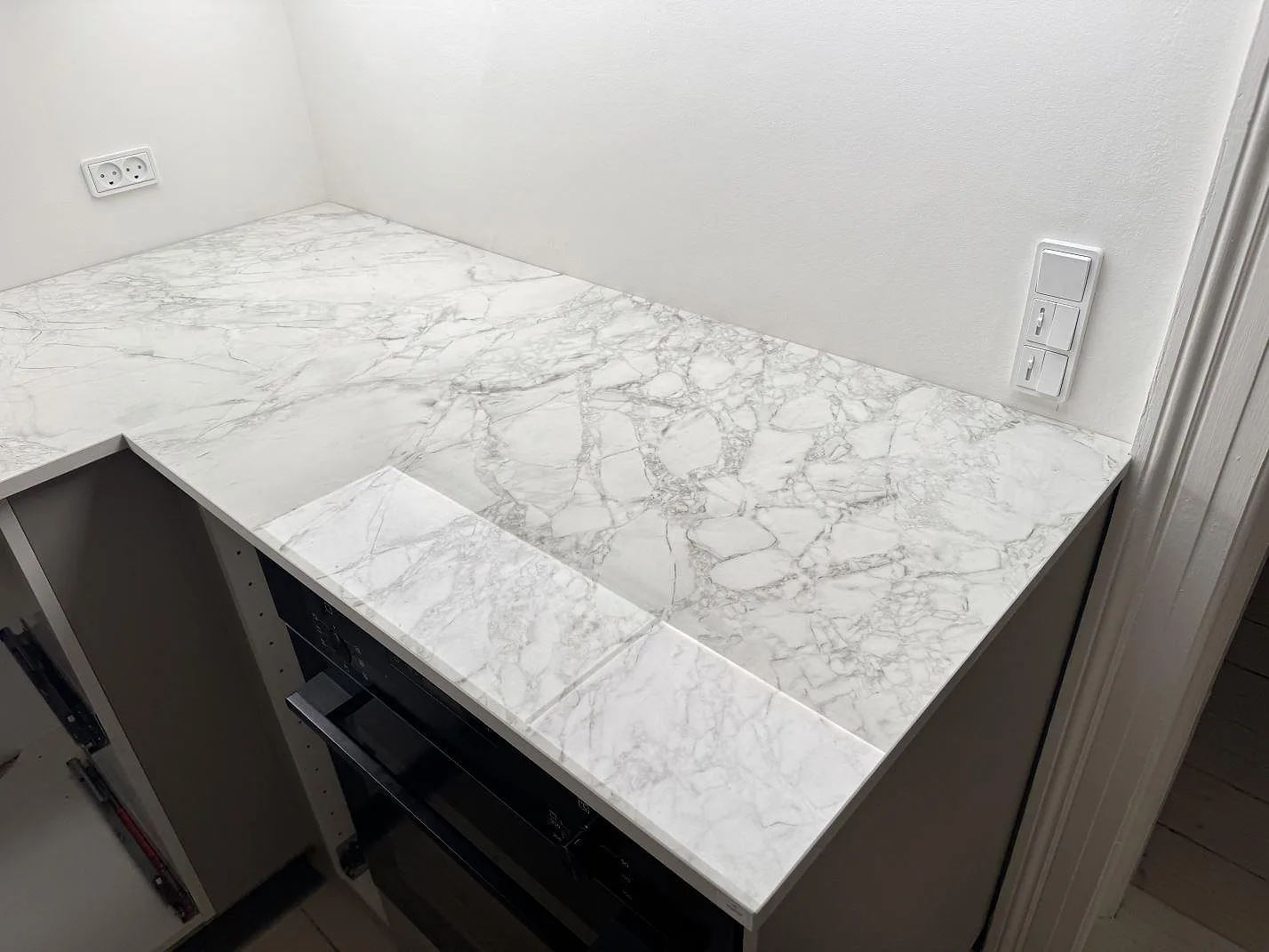 Polerad köksbänkskiva i Dekton Bergen keramik längs vägg och ugnssektion i ett kök i Frederiksberg.