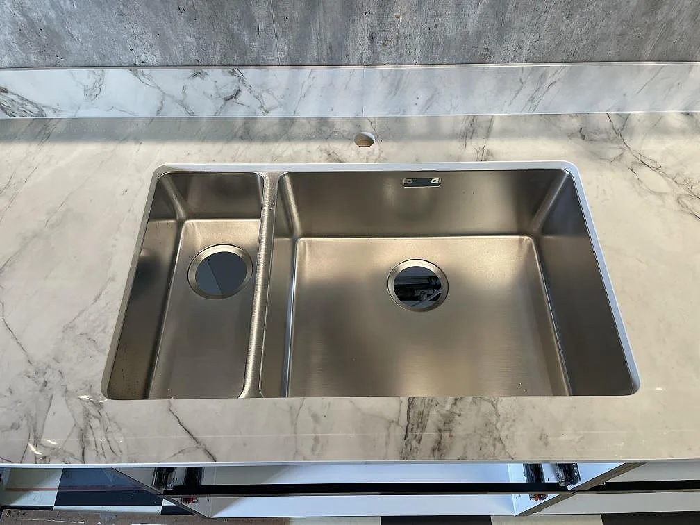 Närbild på polerad Dekton Bergen som köksbänkskiva med rostfri diskho och låg stänkkant i Gustavsberg.