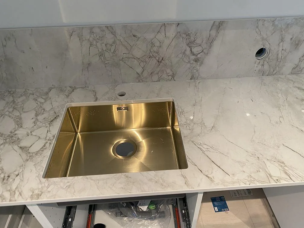 Underlimmad diskho i mässingston i köksbänkskiva av polerad Dekton Bergen med marmorlik grå ådring, kök i Hjärup.