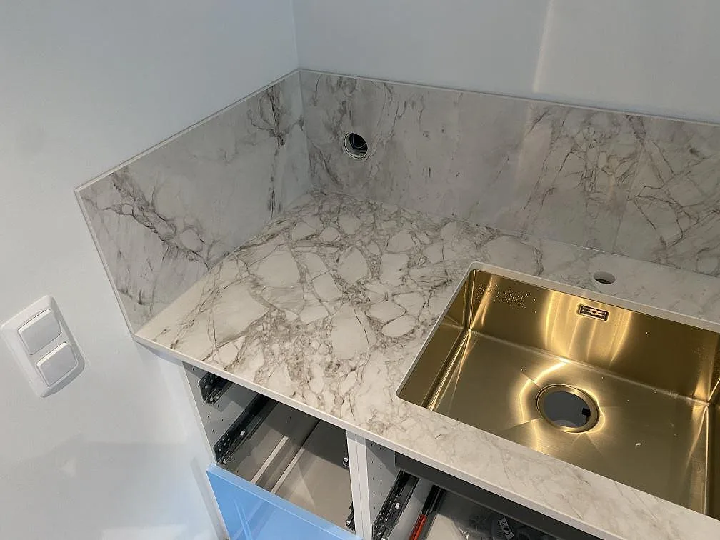 Hörnsektion av köksbänkskiva i Dekton Bergen med underlimmad mässingston diskho och stänkskydd, polerad keramik i ett kök i Hjärup.