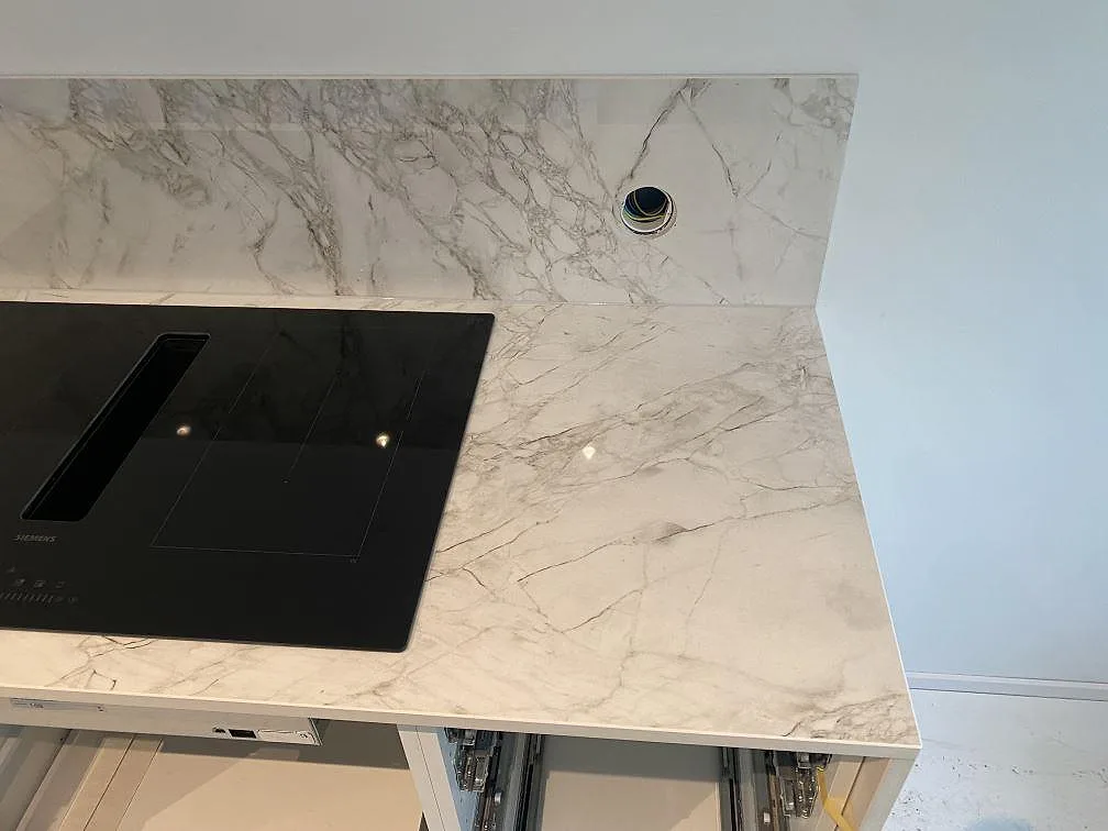 Infälld induktionshäll och blandarhål i polerad Dekton Bergen köksbänkskiva med uppvikt stänkskydd, kök i Hjärup.
