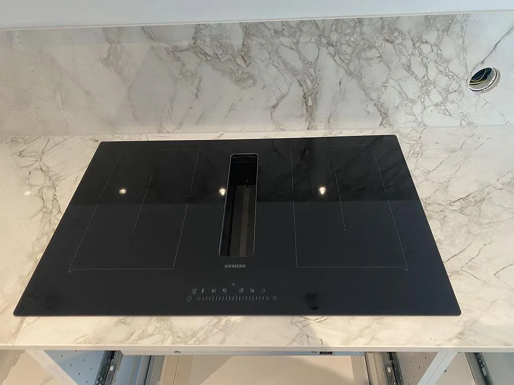 Infälld Siemens induktionshäll i polerad Dekton Bergen köksbänkskiva med uppvikt stänkskydd i samma sten, kök i Hjärup.
