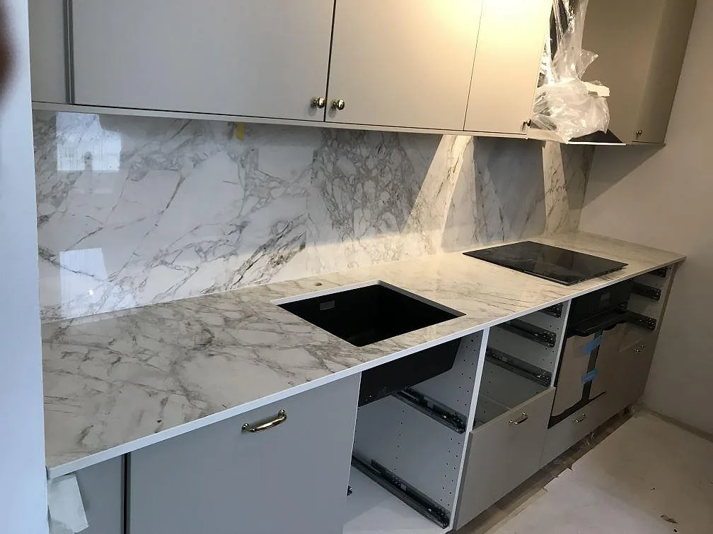 Köksbänkskiva i vit ådrad Dekton Bergen, polerad, med heltäckande stänkvägg, underlimmad svart kompositdiskho och infälld induktionshäll i ett kök i Malmö.