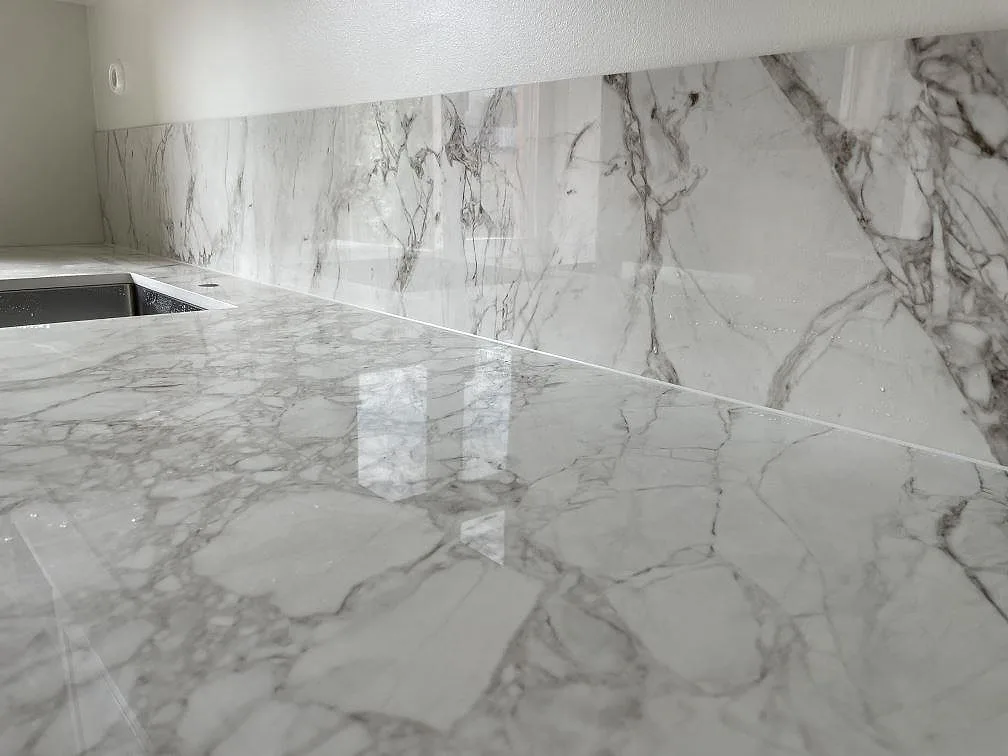 Detalj av blank Dekton Bergen bänkskiva och stänkskydd med marmorerad ådring under köksmontering i Stockholm.
