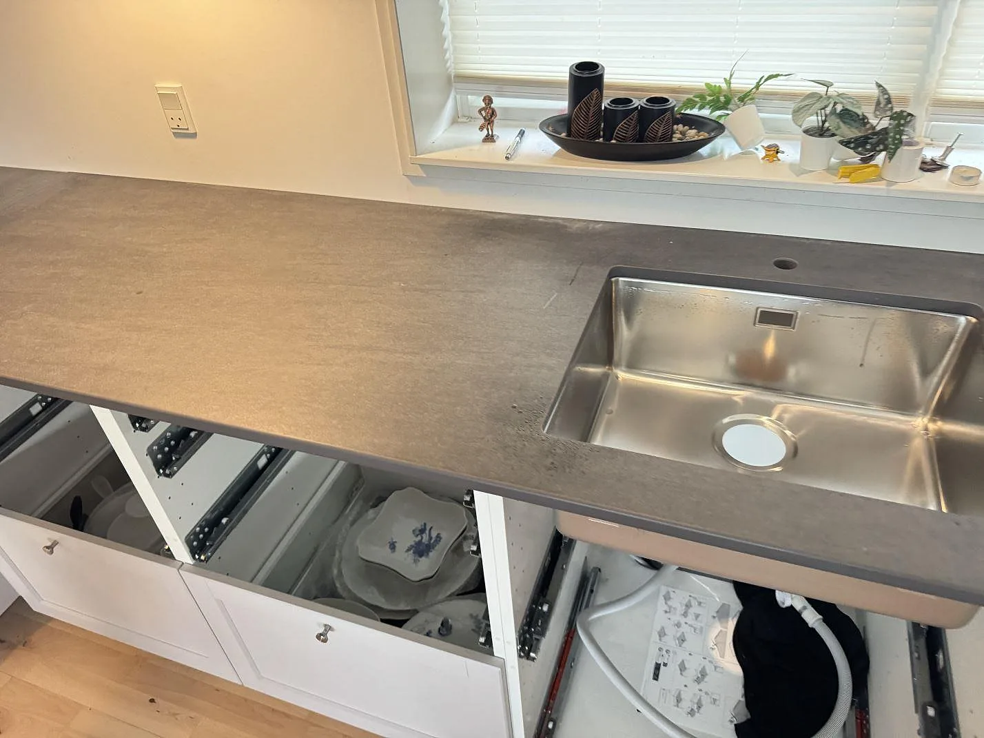 Lång bänkskiva i matt Dekton Bromo med rostfri diskho och öppna köksstommar under montering i 3500 Værløse.