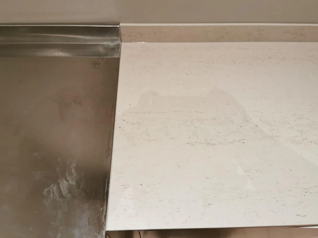 Bänkskiva i Dekton Danae i matt utförande där stenytan möter ett rostfritt stänkskydd i ett kök i Åhus.