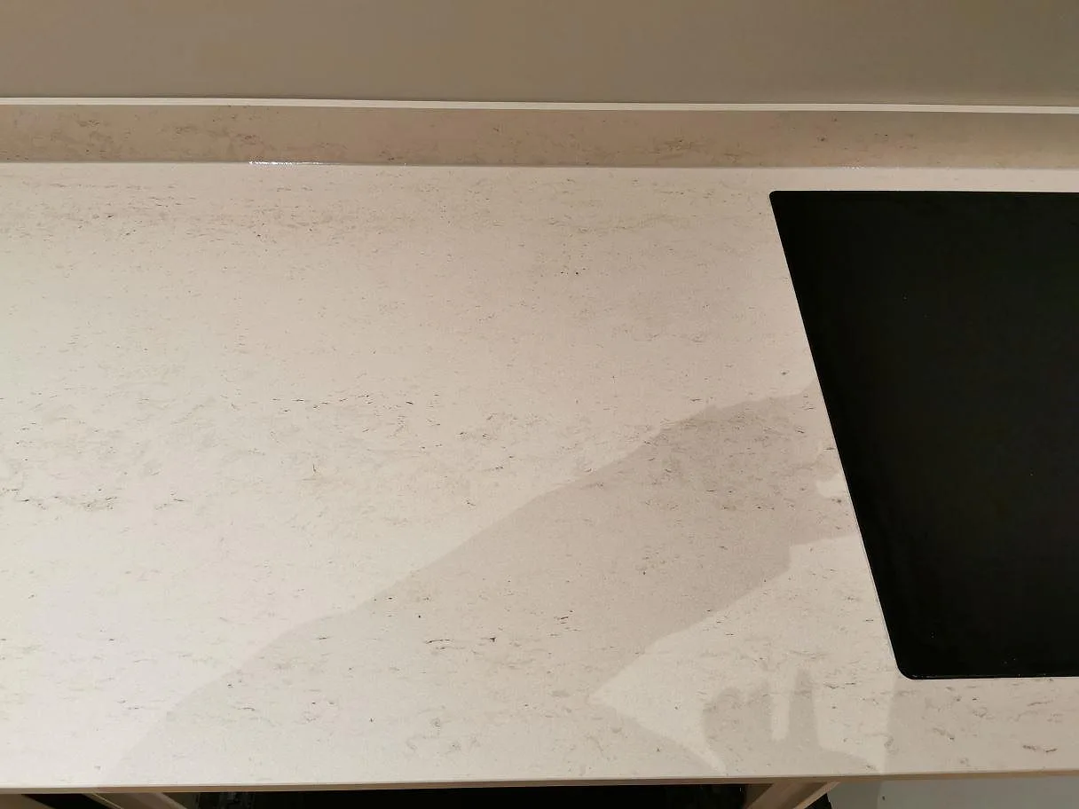 Matt köksbänkskiva i Dekton Danae med mjuk beige ådring och kanten av en infälld induktionshäll i Åhus.