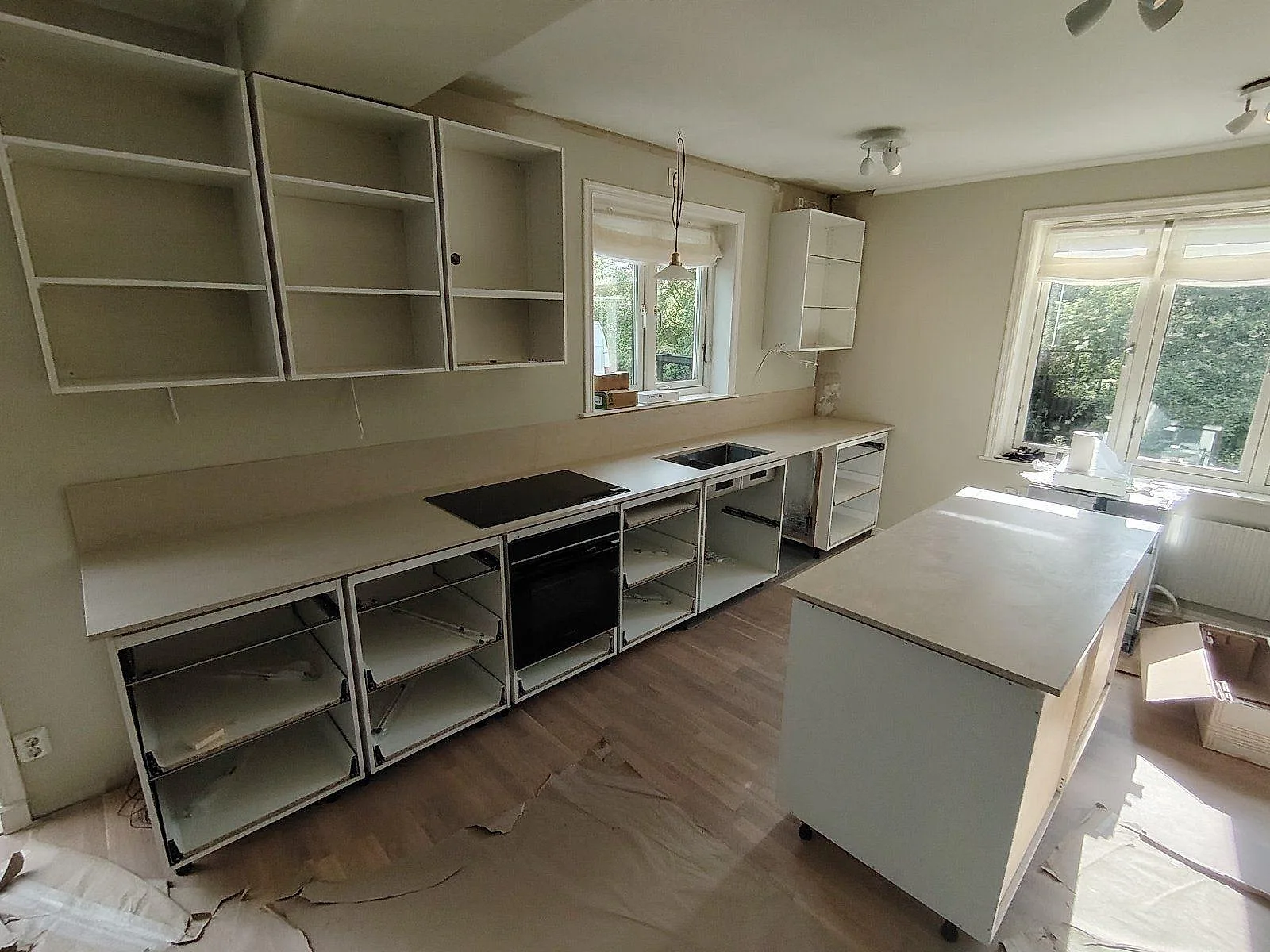 Köksbänkskiva och köksö i matt Dekton Danae, beige keramik, med svart induktionshäll och lågt stänkskydd i ett kök under montering i Bromma.