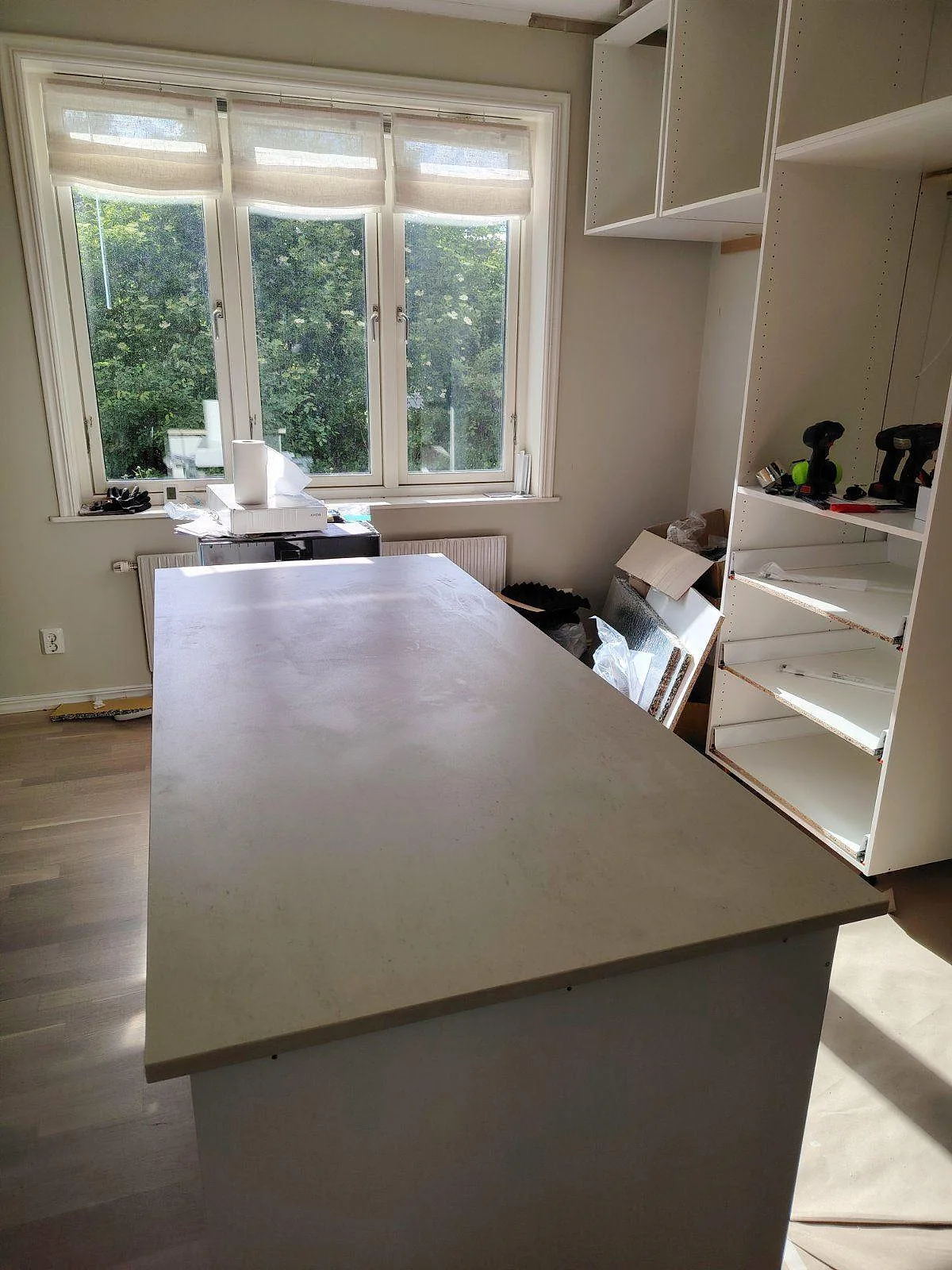 Köksö i matt Dekton Danae, beige keramik med lugn ådring, framför stora fönster och vita köksstommar under montering i Bromma.