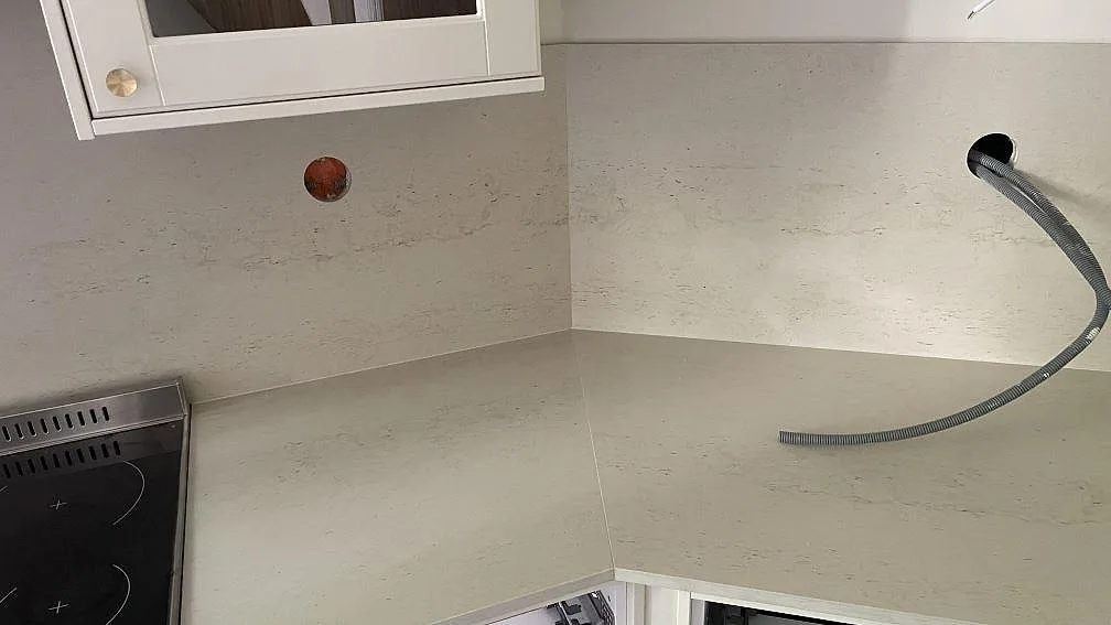 Hörnparti med matt Dekton Danae som bänkskiva och väggbeklädnad, med ljus beige stenstruktur i ett kök i Göteborg.