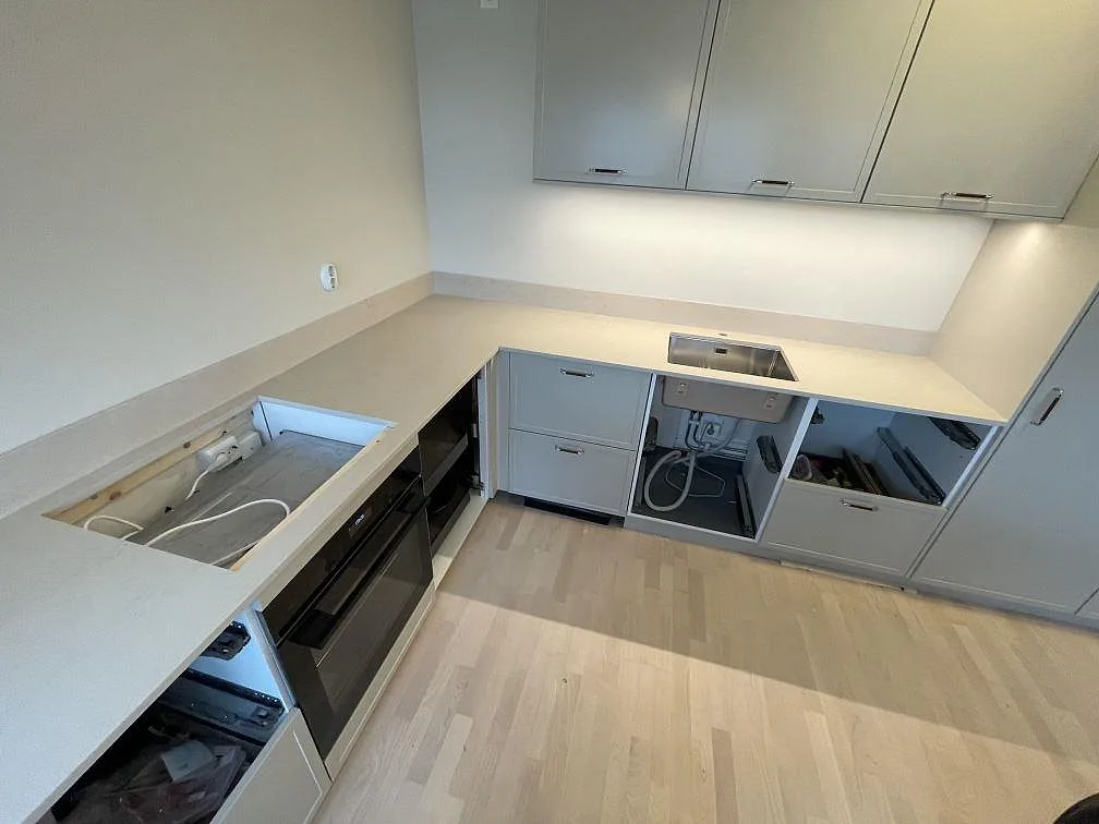 Köksbänkskiva i matt Dekton Danae, ljus keramik, med hällöppning, underlimmad rostfri diskho och lågt stänkskydd i ett kök i Hägersten.
