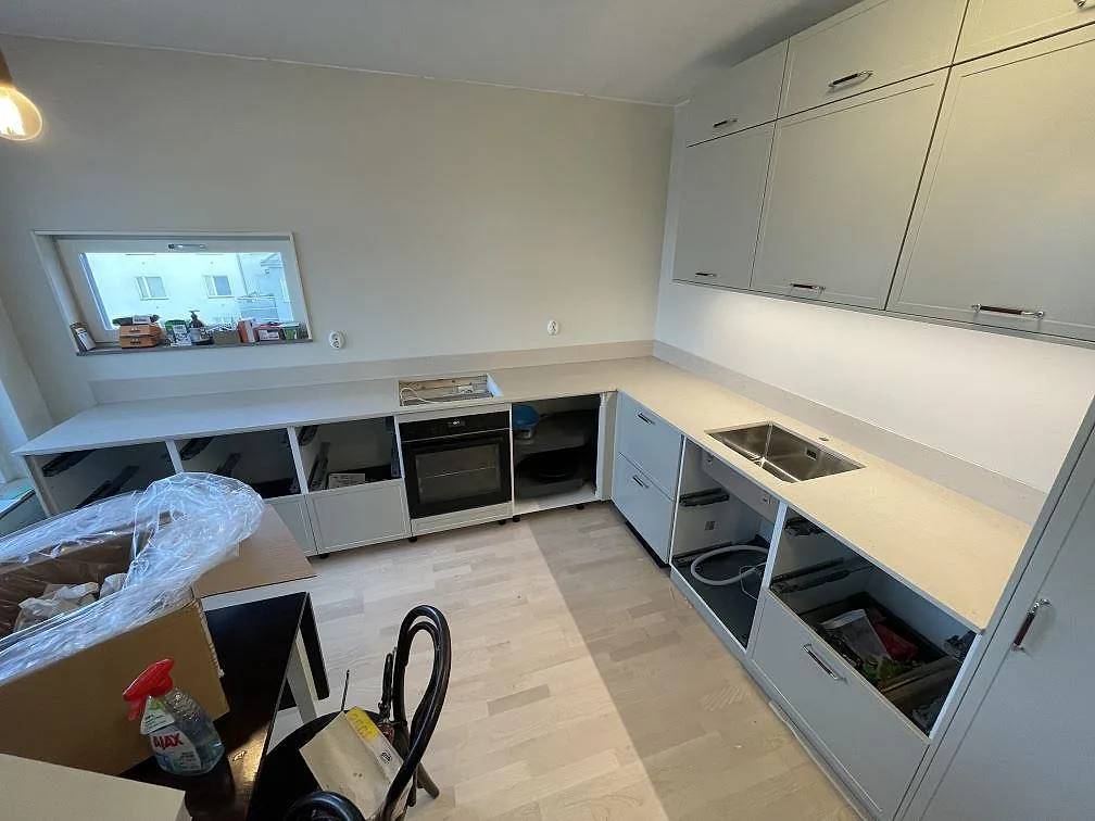 Vinkelkök i Hägersten med monterade bänkskivor i matt Dekton Danae, rostfri diskho och ljus väggstänkkant under montering.