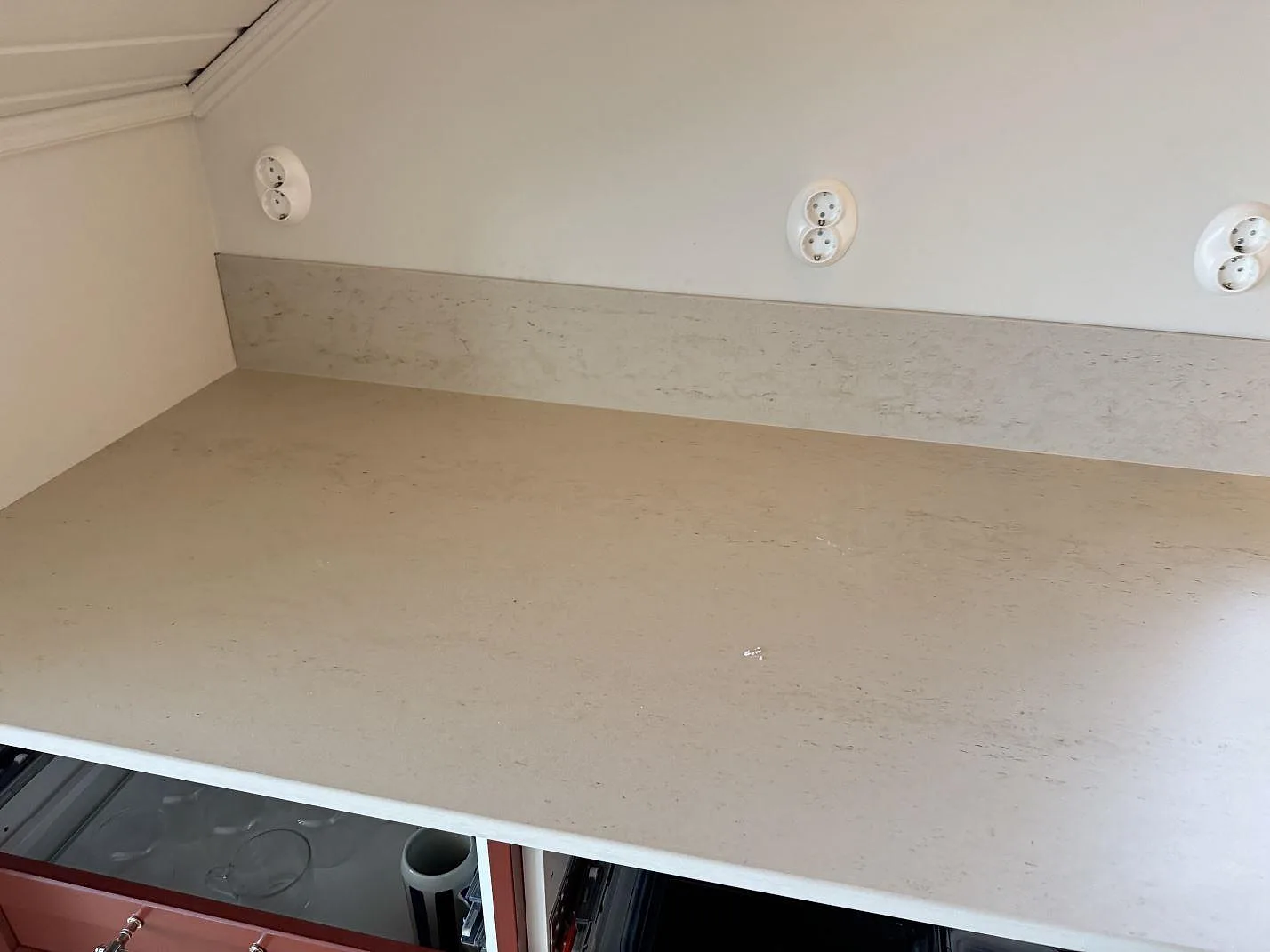 Lång arbetsyta i matt Dekton Danae keramik med uppvikt stänkskydd och röda köksluckor i Hakenäset.