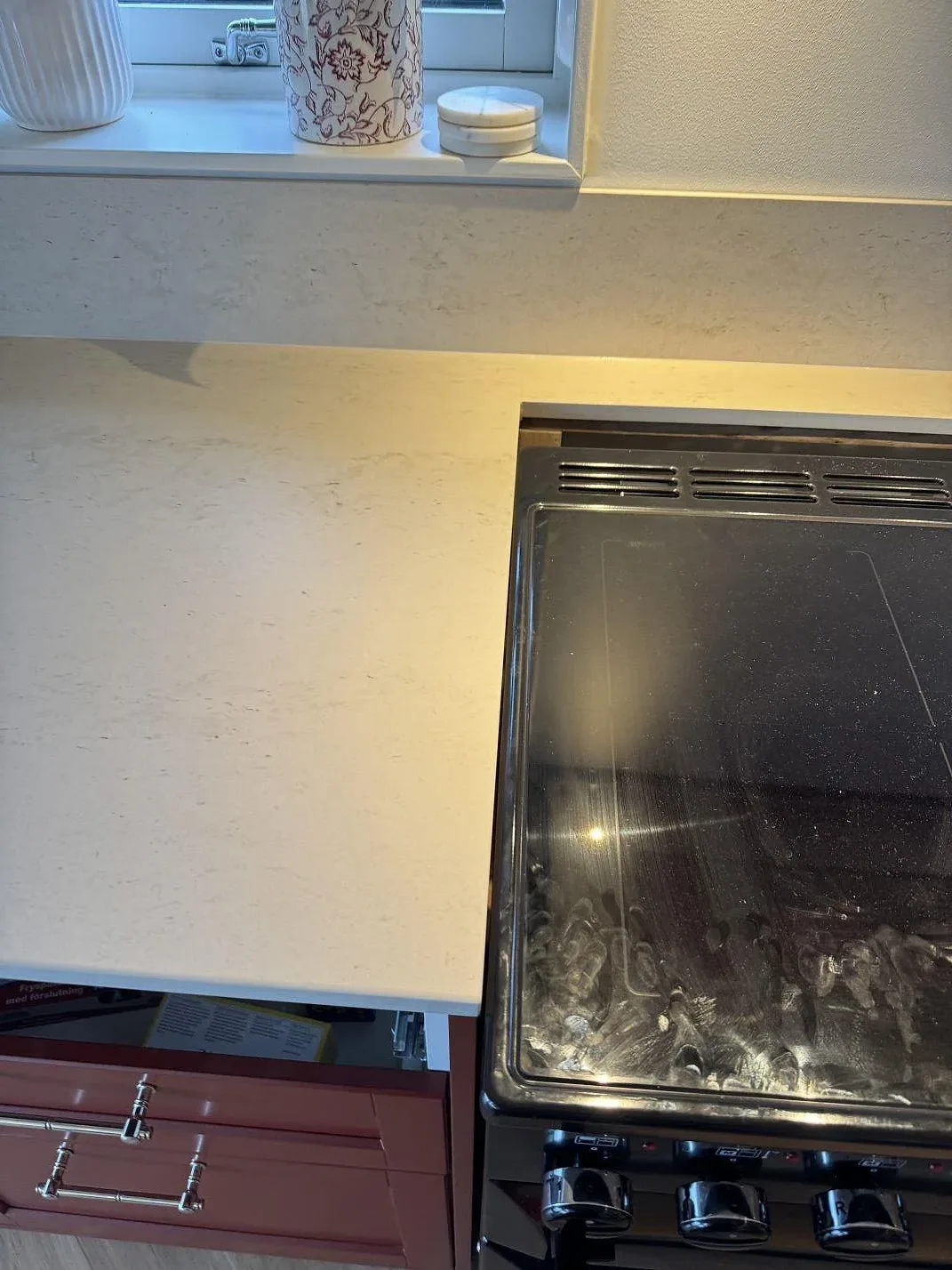 Detalj av matt Dekton Danae keramik runt hällen, med fönster och röda köksluckor i Hakenäset.