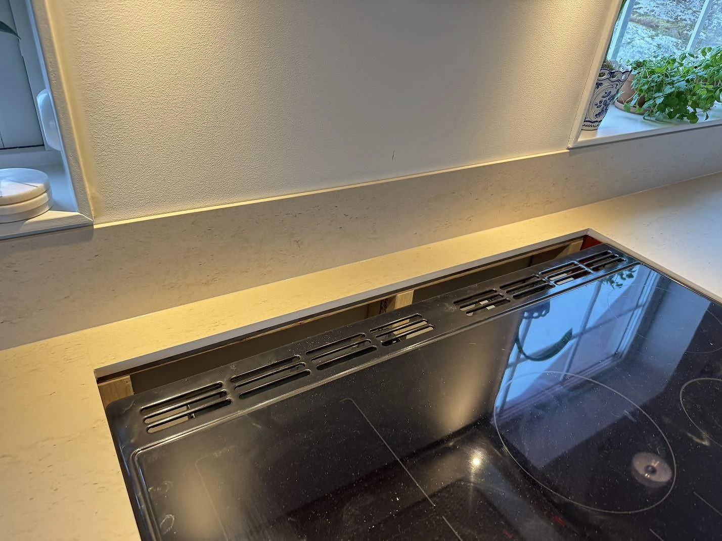 Hällområde med matt Dekton Danae keramik, uppvikt stänkskydd och svart häll under fönster i Hakenäset.